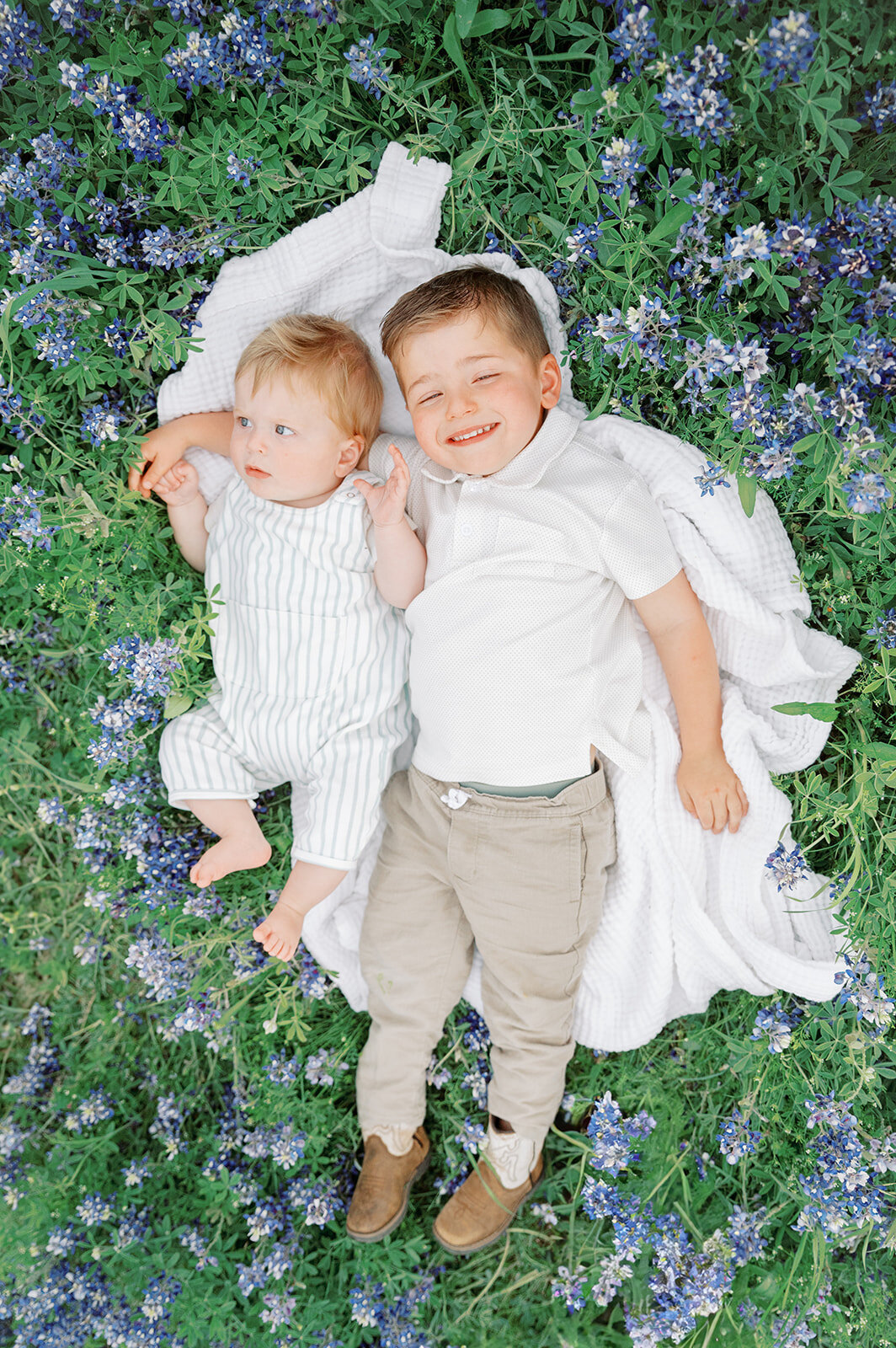 Brother's laying on a white blanket in a field of bluebonnets wearing coordinating clothing