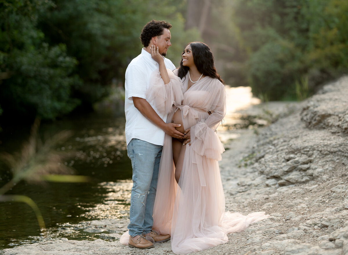 pregnant couple standing together by a creek