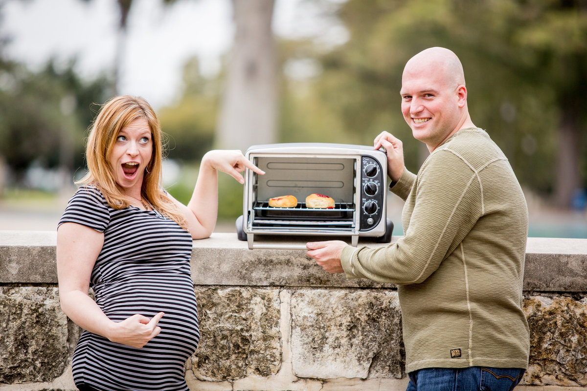 Twins Maternity session of woman and man pointing at buns in the oven at San Pedro Park in San Antonio.