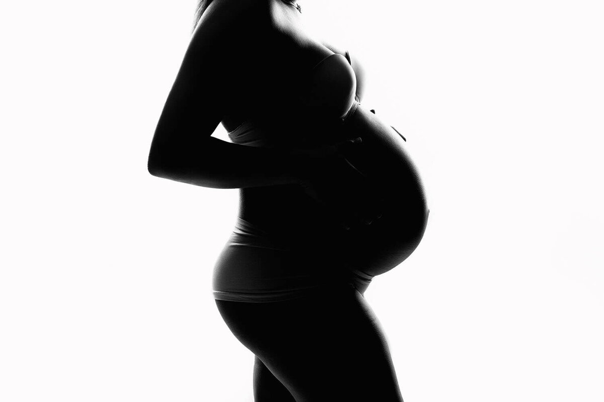 Silhouette of a pregnant woman standing in a studio in underwear with hands on her bump taken by a New Orleans Maternity Photographer