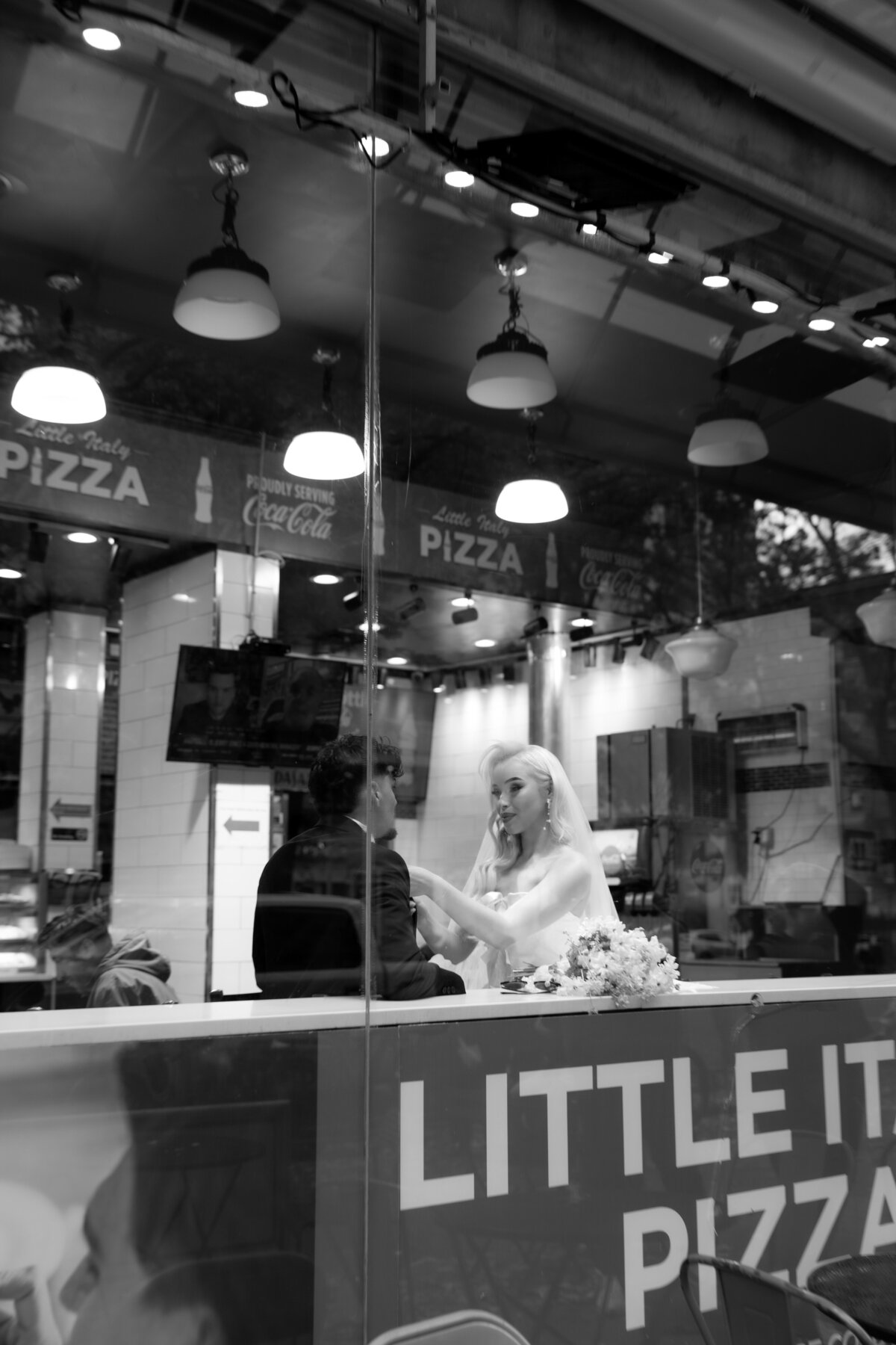 A candid moment of the couple chatting and eating pizza inside a busy NYC pizza shop.