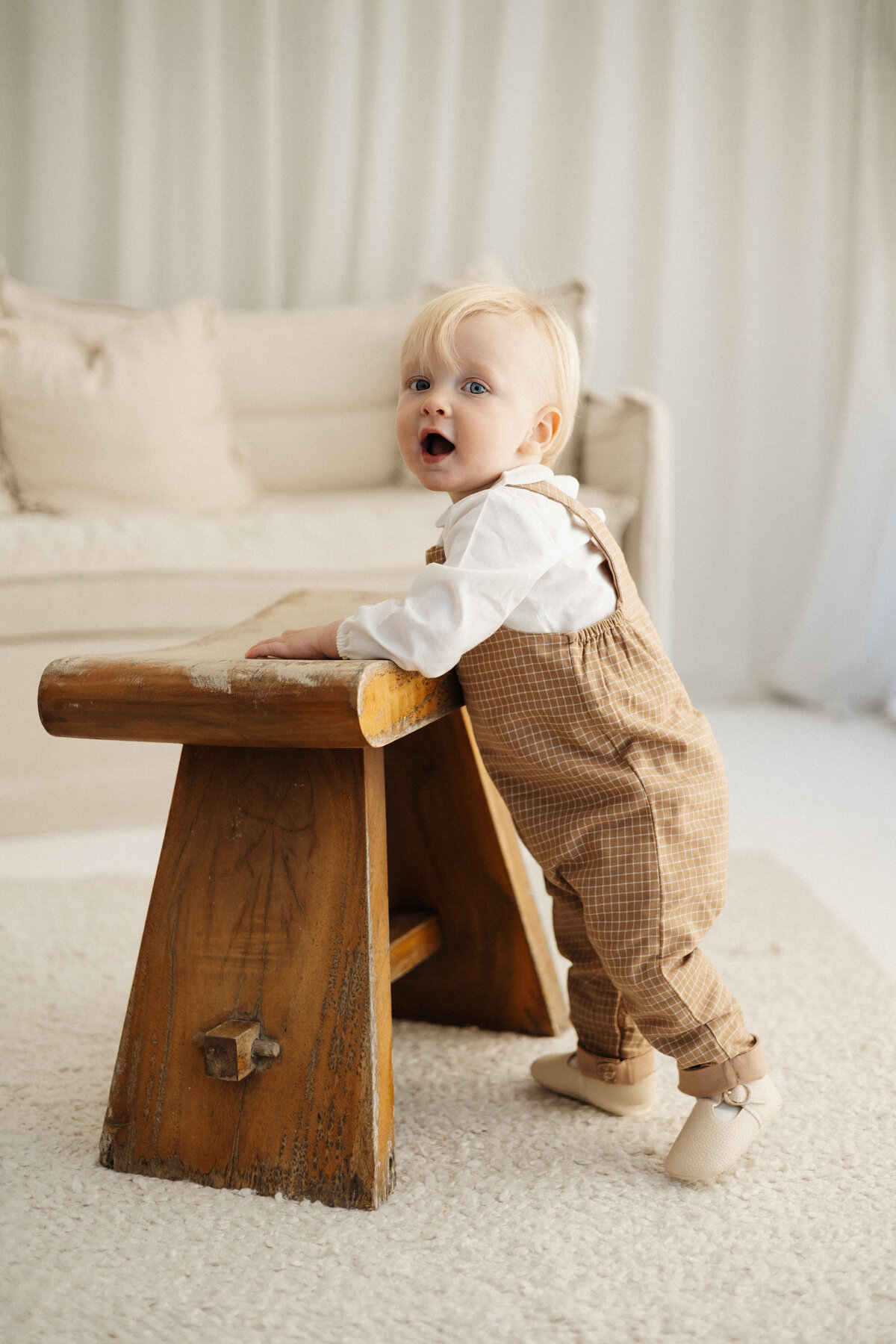 A little baby boy holding onto a bench seat for support during his milestone photoshoot in a christchurch newborn photography studio