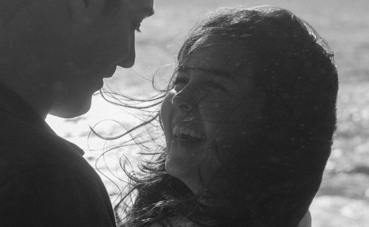 windy Oregon Coast engagement photo with couple cuddled close and smiling at each other