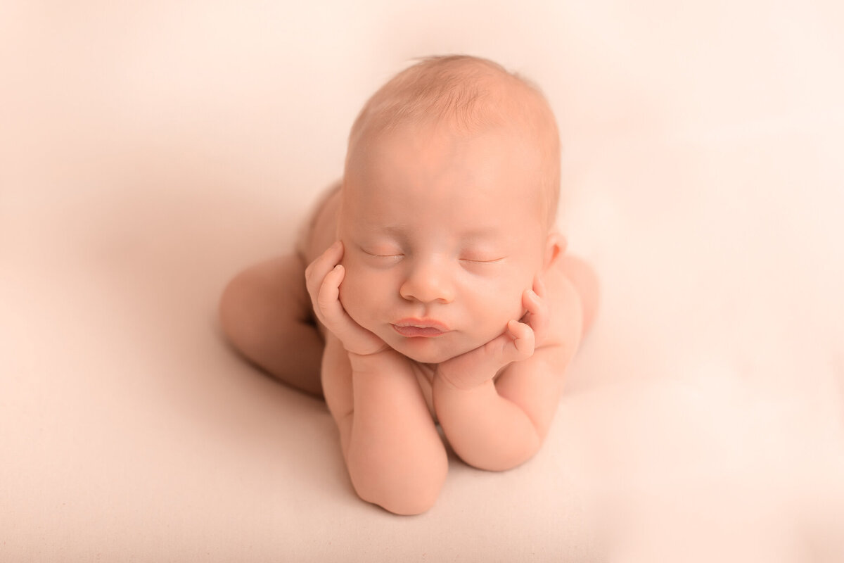 Nyfödd bebis i froggy pose med beige bakgrund