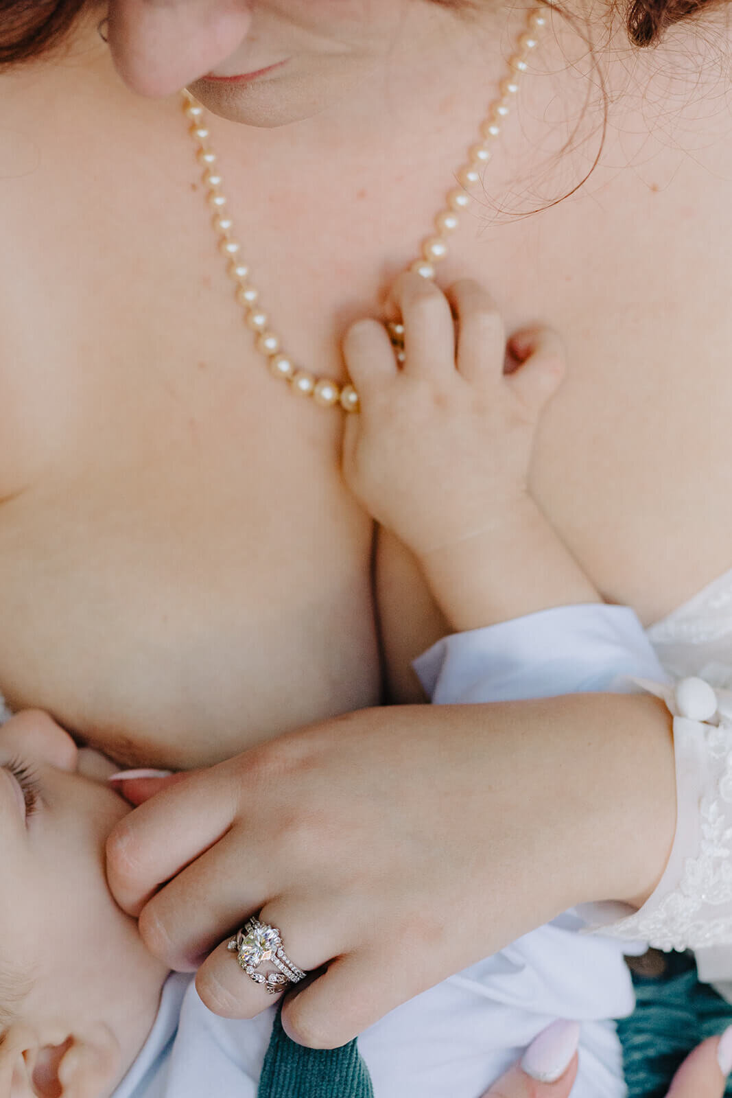 close of babies hand reaching for moms pearl necklace