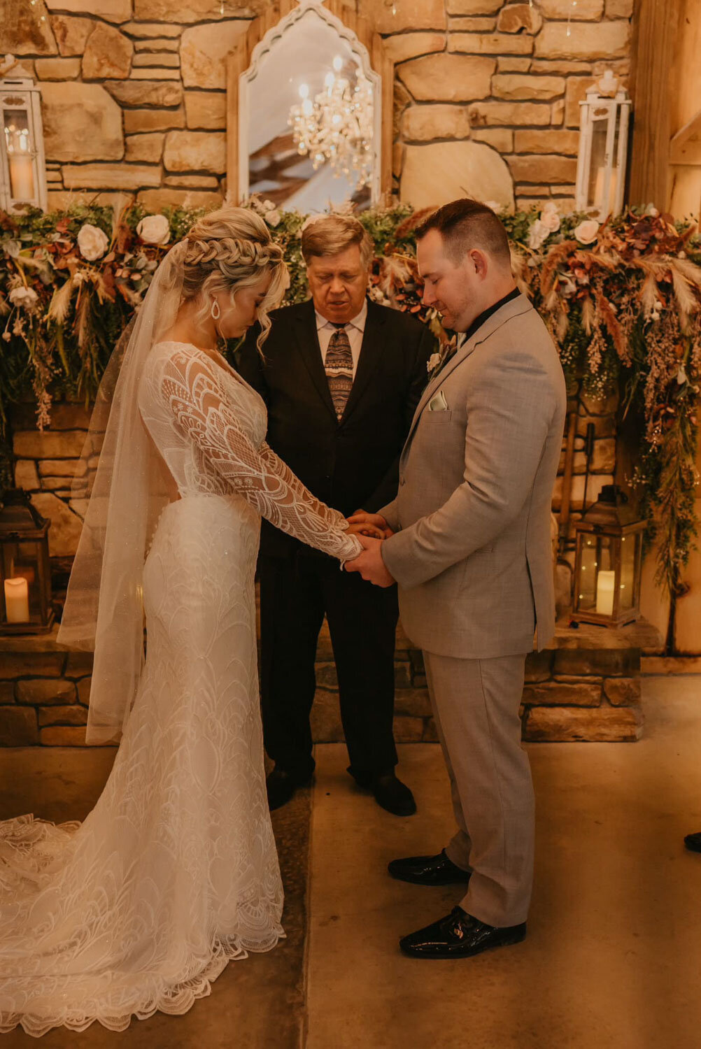 Bride and groom holding hands during their wedding ceremony in front of a rustic stone fireplace