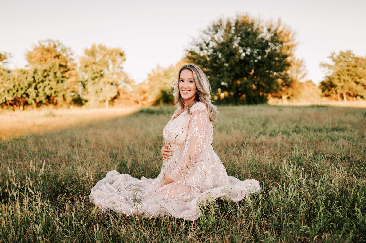 maternity photo of pregnant mom kneeling and smiling in field in Springfield MO