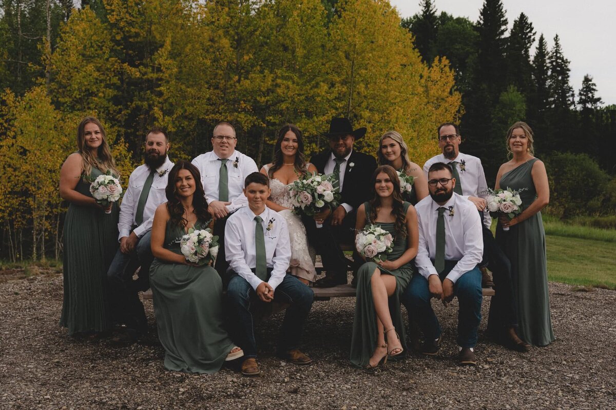 Bridal party sitting on a picnic table in front of fall colours