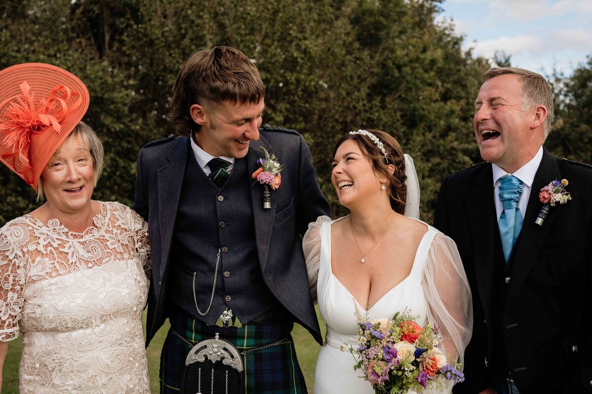 A bride and groom are photographed linking arms with their family members. They smile candidly in an Aberdeenshire field