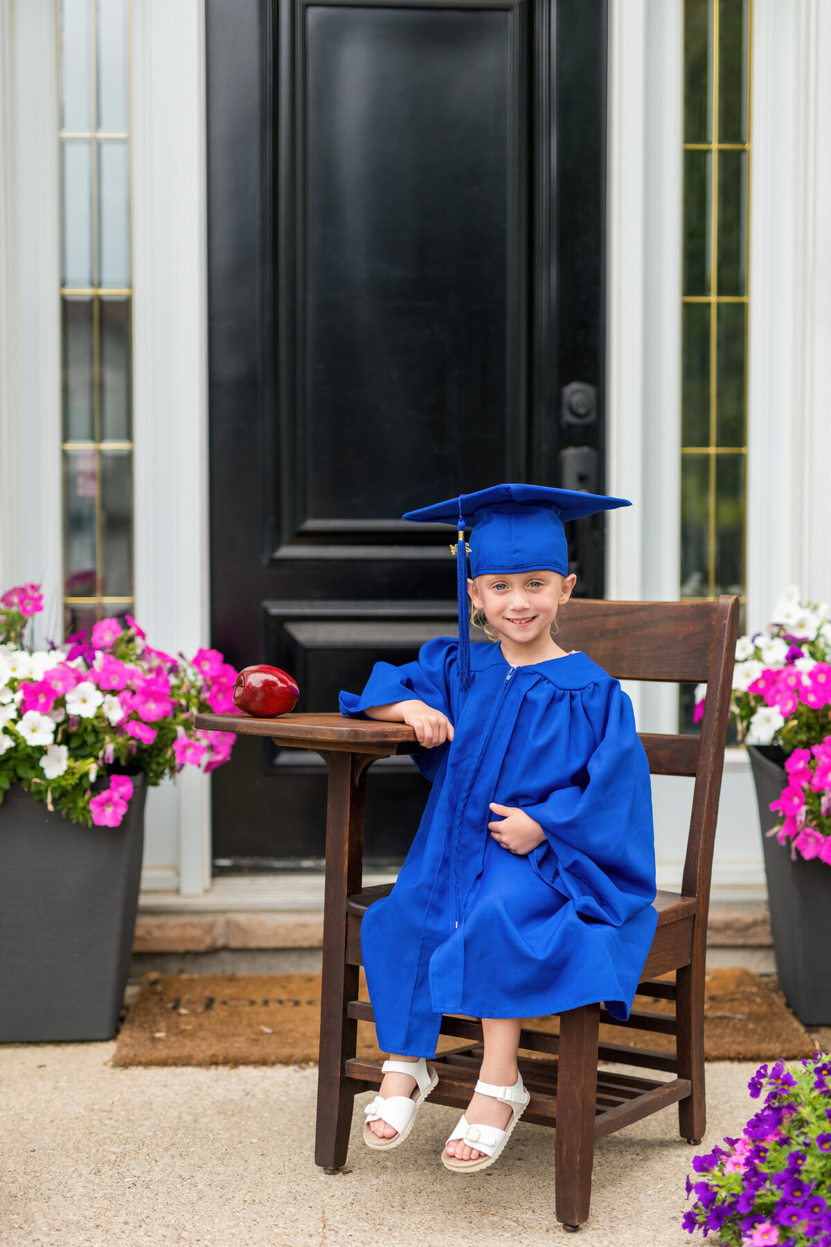 Child grad milestone photo with apple and wooden chair—celebrating a new chapter with a timeless smile.