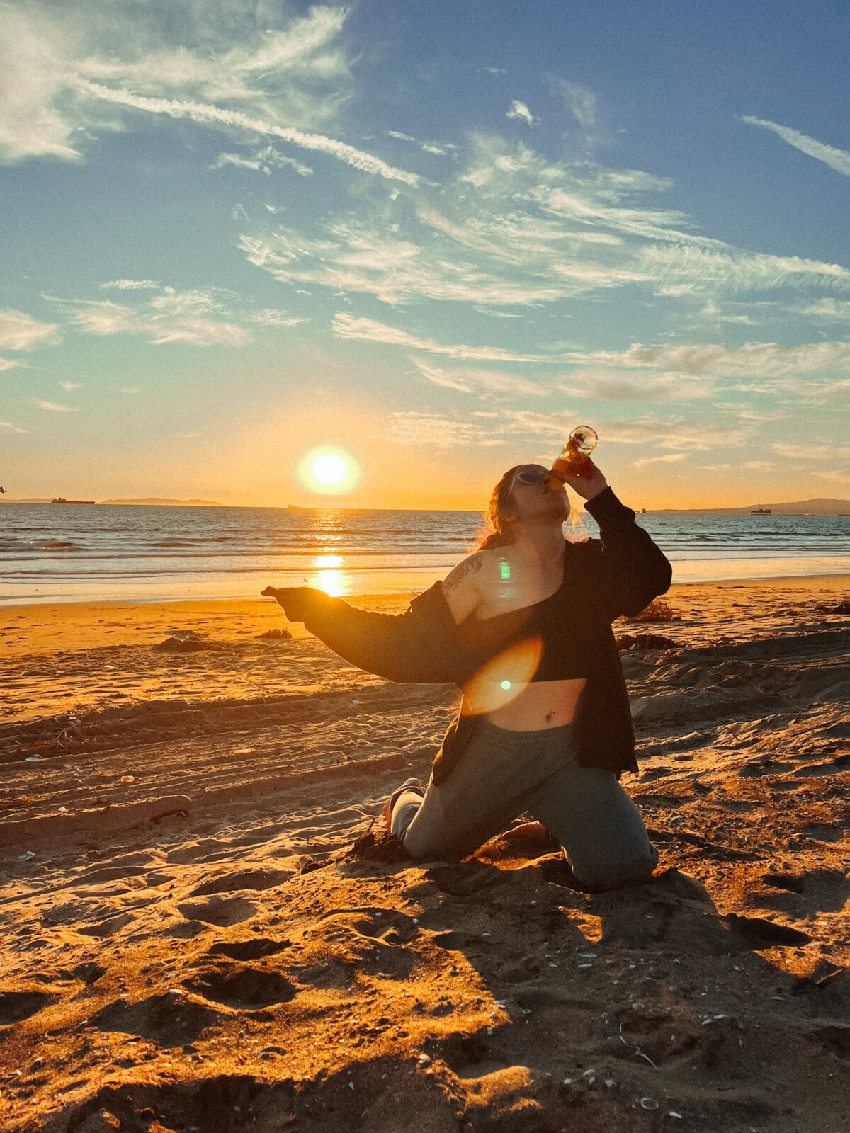 A Colorado elopement photographer kneels on a beach drinking a beer.