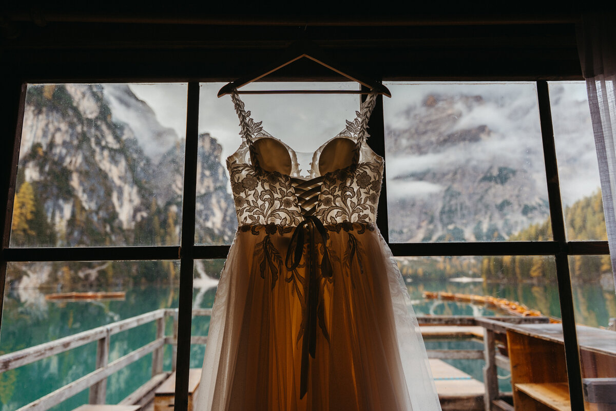Detailed beaded wedding dress hanging by lake cabin window