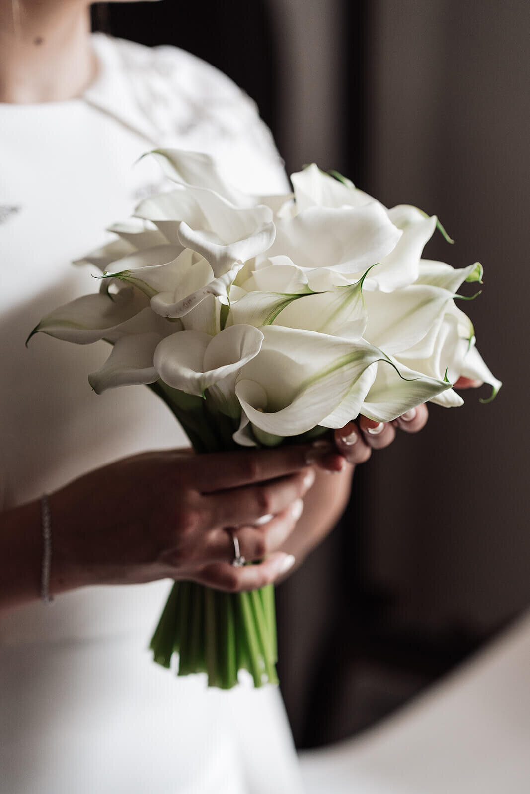 closeup of a bouquet of white calla lilies being held by a bride in her wedding dress on the morning of her intimate london wedding at the nomad hotel