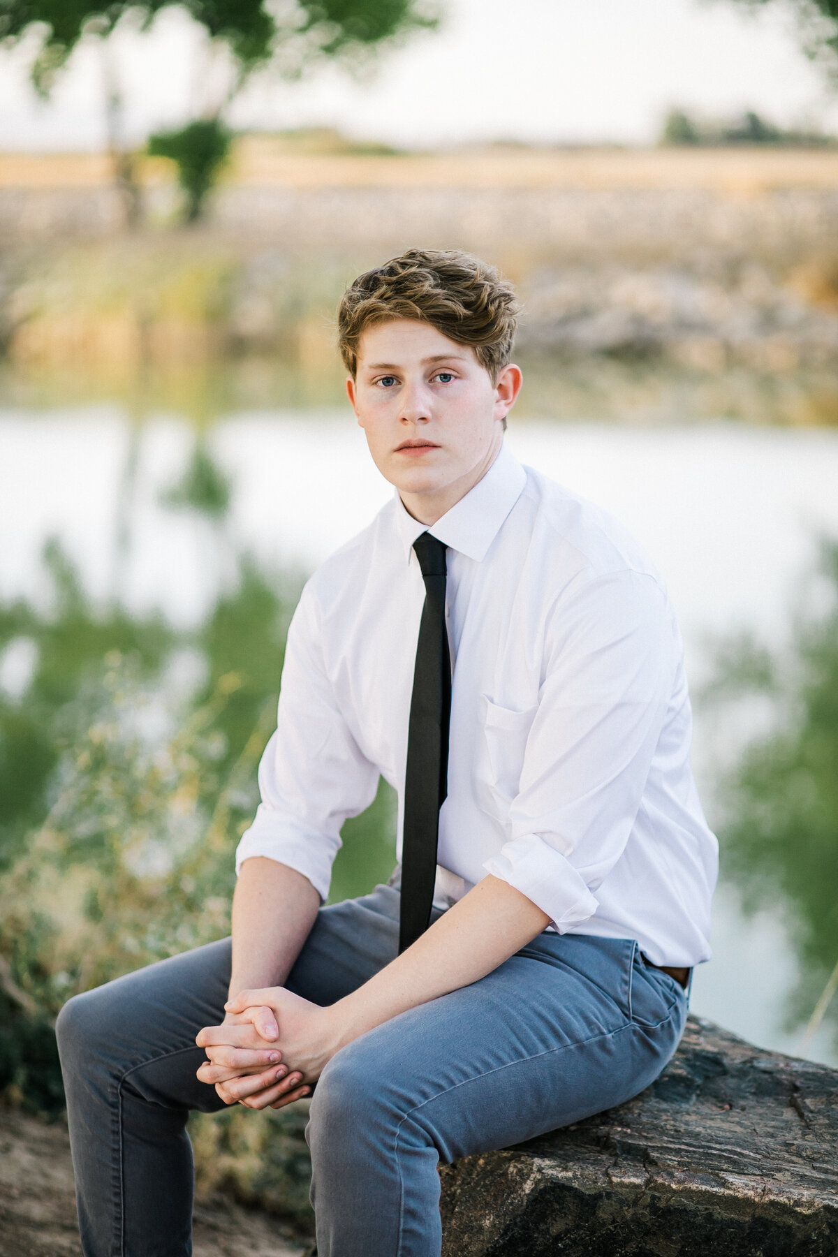 young man sits on a rock by a pond