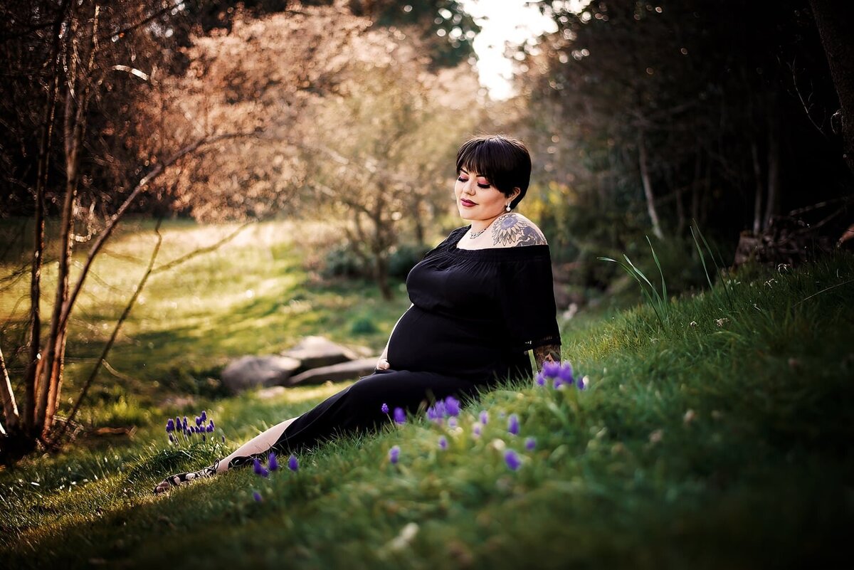 Pregnancy photos with mom in black dress sitting on grass