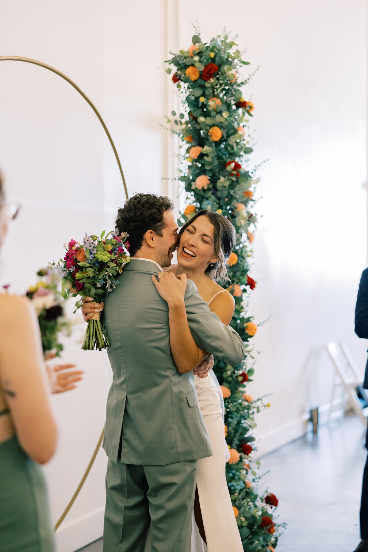 Brendan and Sara kissing under floral arch by Crimson & Clover during Fetewell wedding ceremony in Baltimore.
