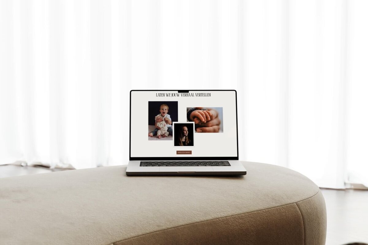 Laptop placed on a light beige ottoman in front of white curtains, showing a photography website section with newborn baby photos, a close-up of a tiny hand, and a smiling portrait of a woman.