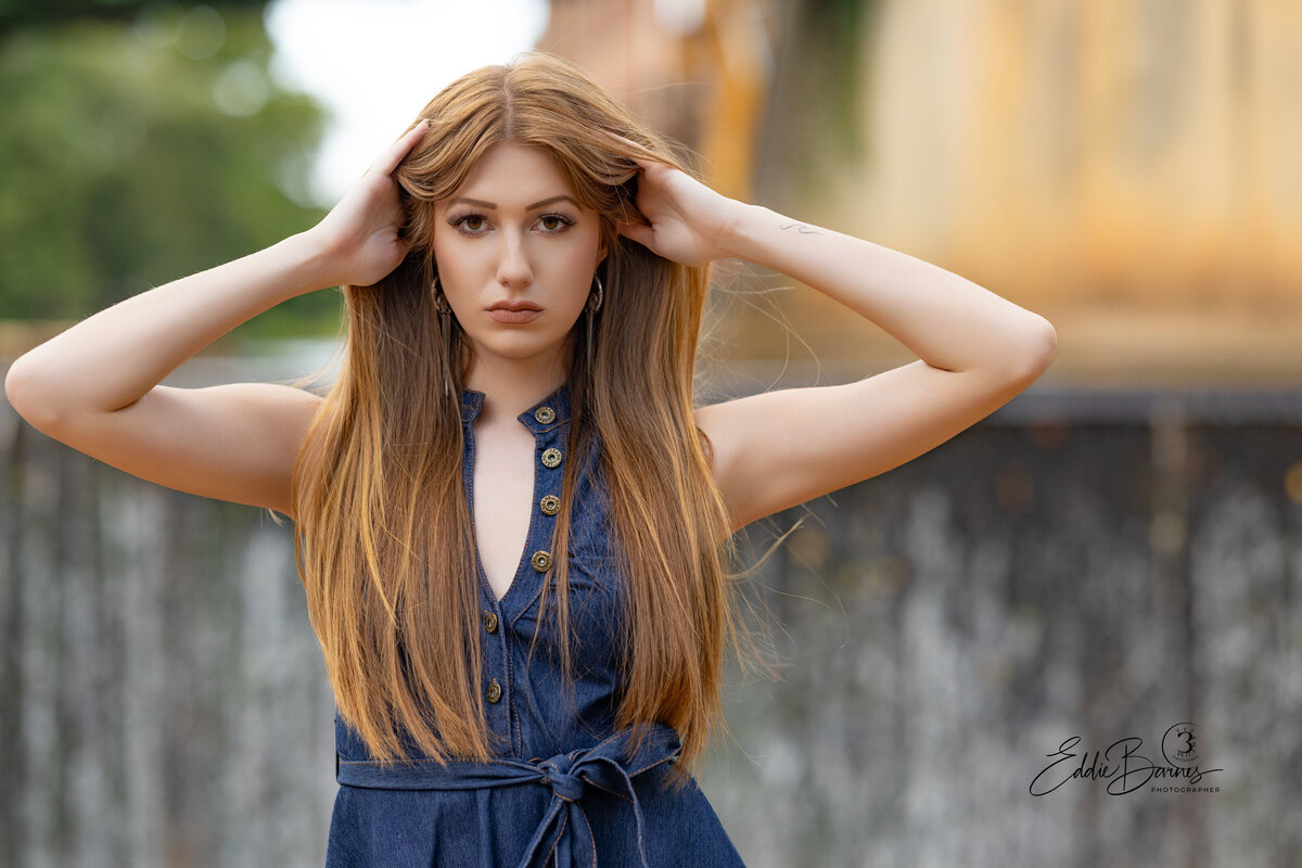 Young woman with long straight hair wearing a denim dress posing confidently outdoors during a professional portrait session in Greenville, SC.