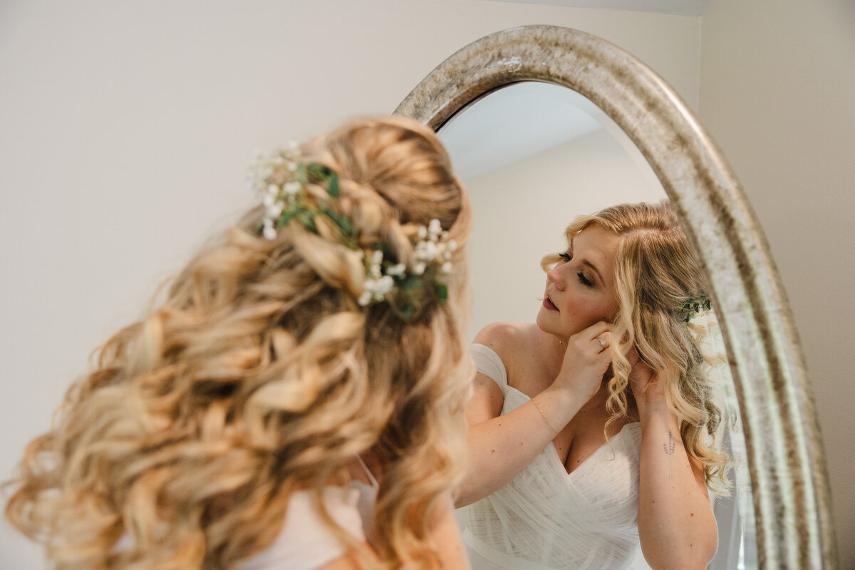 A person seen in a mirror putting in earrings 