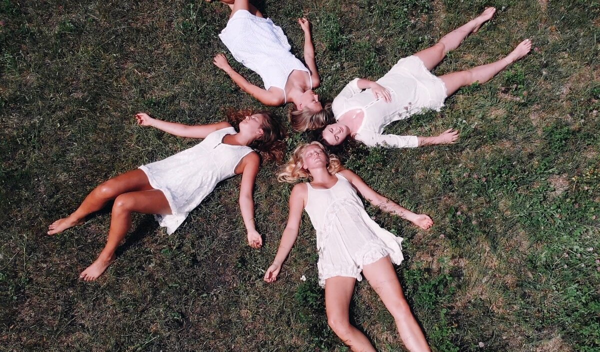 Four women lay  with their heads together on grassy field