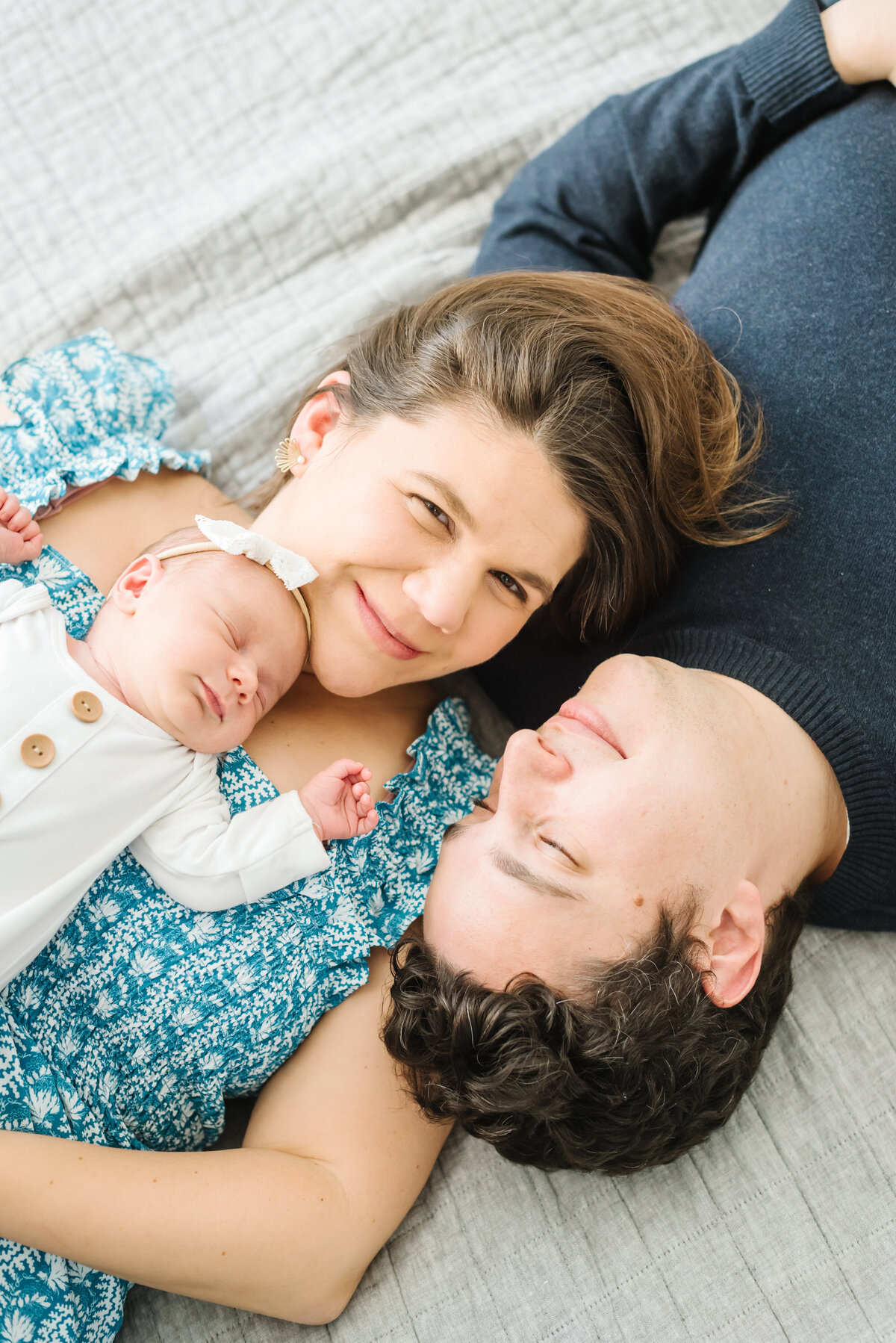 Parents laying on bed with heads together holding newborn - Northern Virginia Newborn Photographer