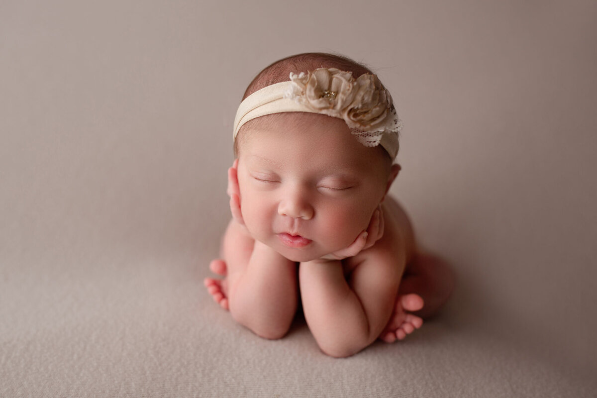 baby girl doing a froggy pose on a cream colored blanket posed by a nj newborn photographer