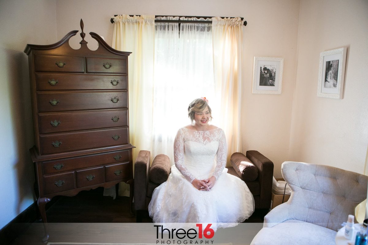 Bride smiles as she sits on a chair prior to the wedding