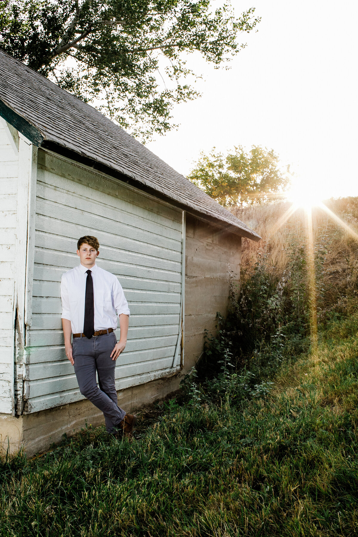a young adult leans against a white barn