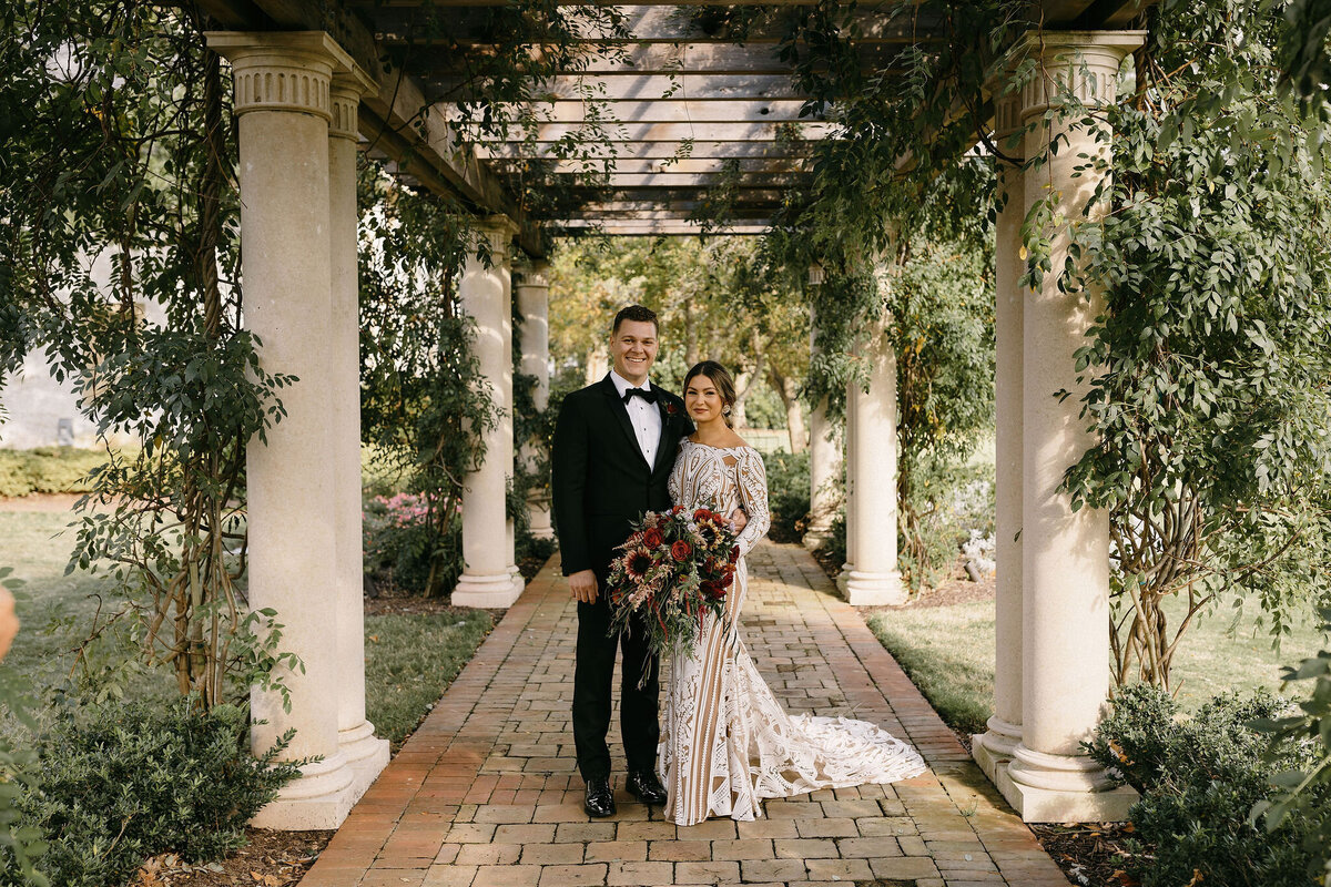 bride and groom standing under pergola in a garden