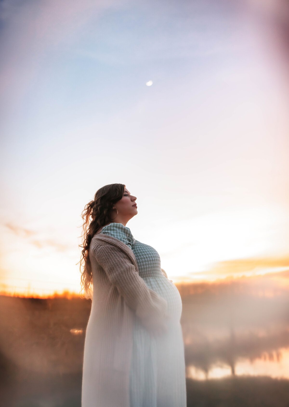 a maternity photo dusk with the moon behind mom holding her bump