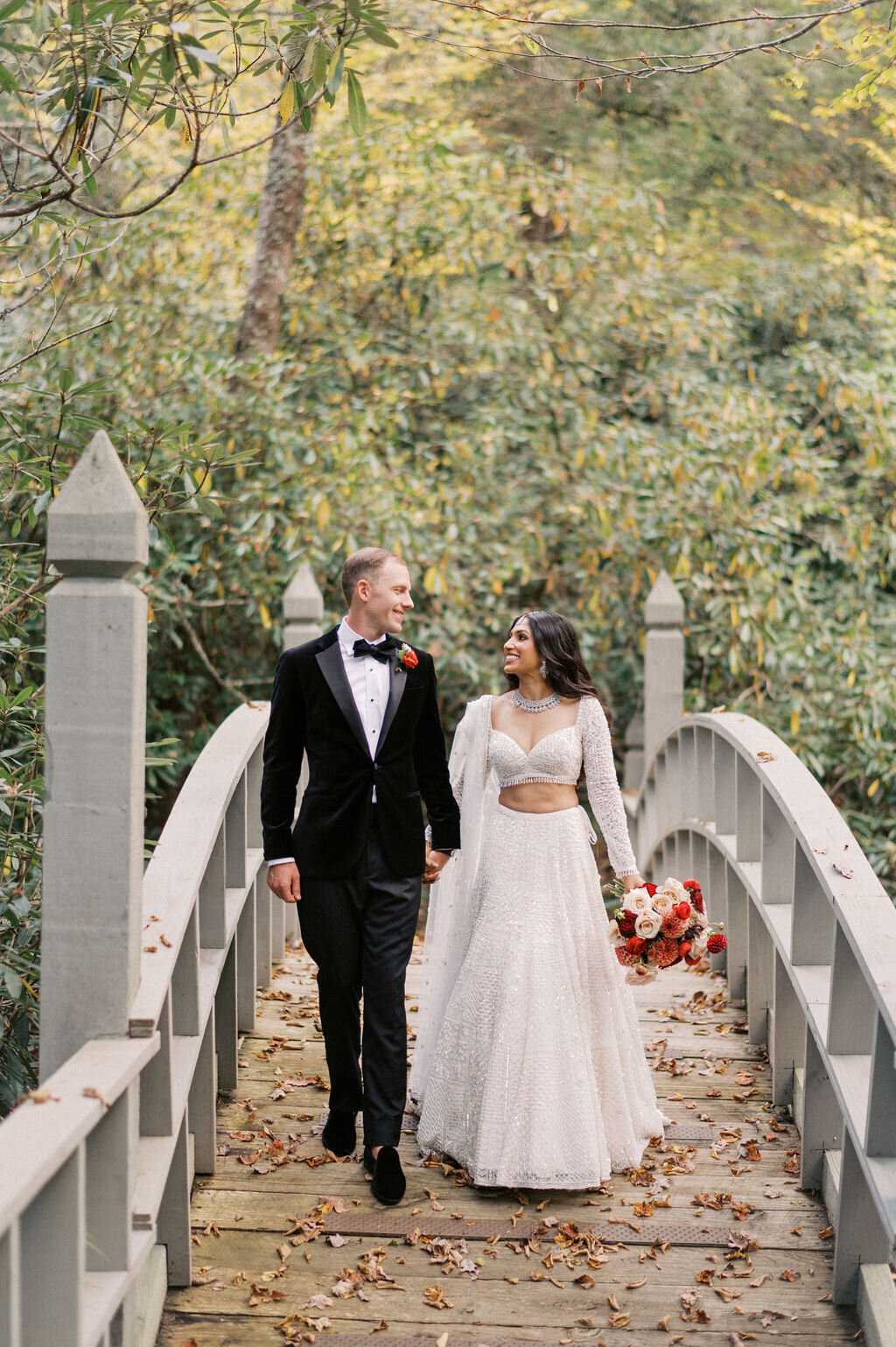 Bride and groom walking hand in hand across the iconic bridge at Old Edwards Inn during their Highlands, NC wedding.