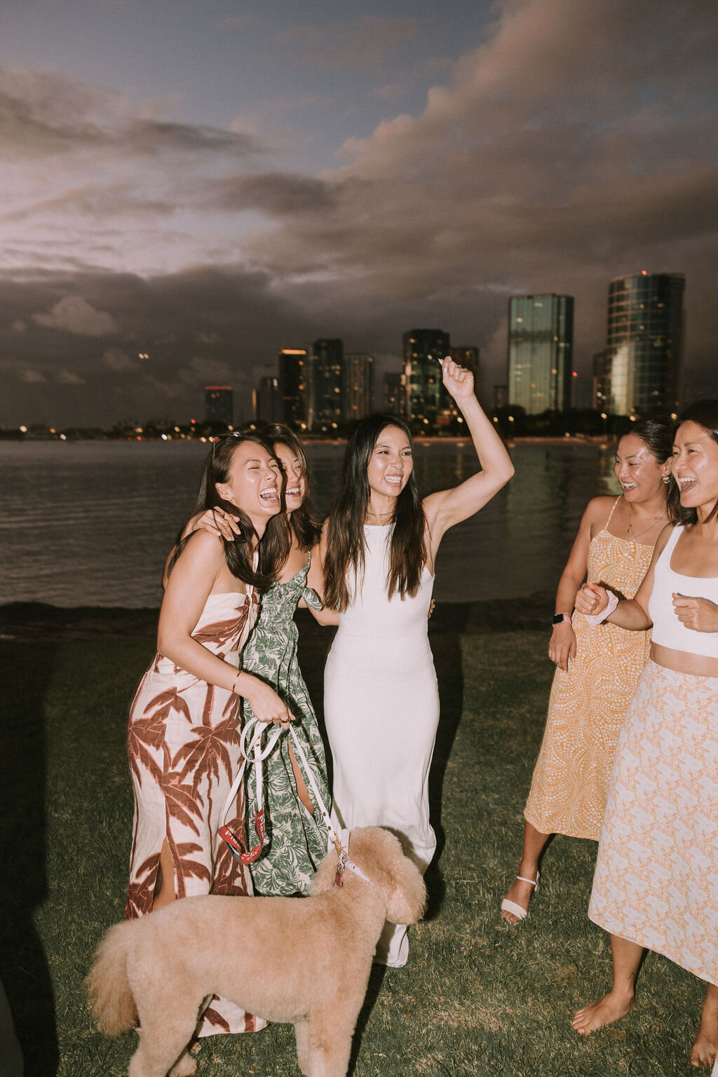 Bride cheering with her girls and dog at welcome dinner in front of the ocean at  dusk