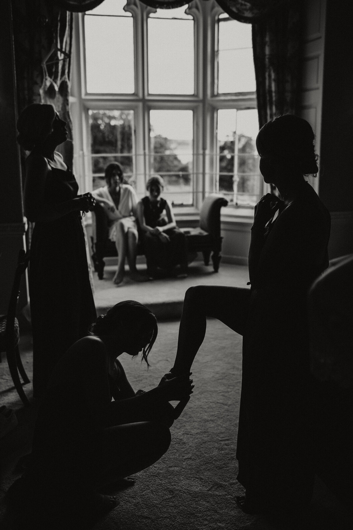 black and whote documentary shot of bridesmaid having shoes put on at Powderham Castle