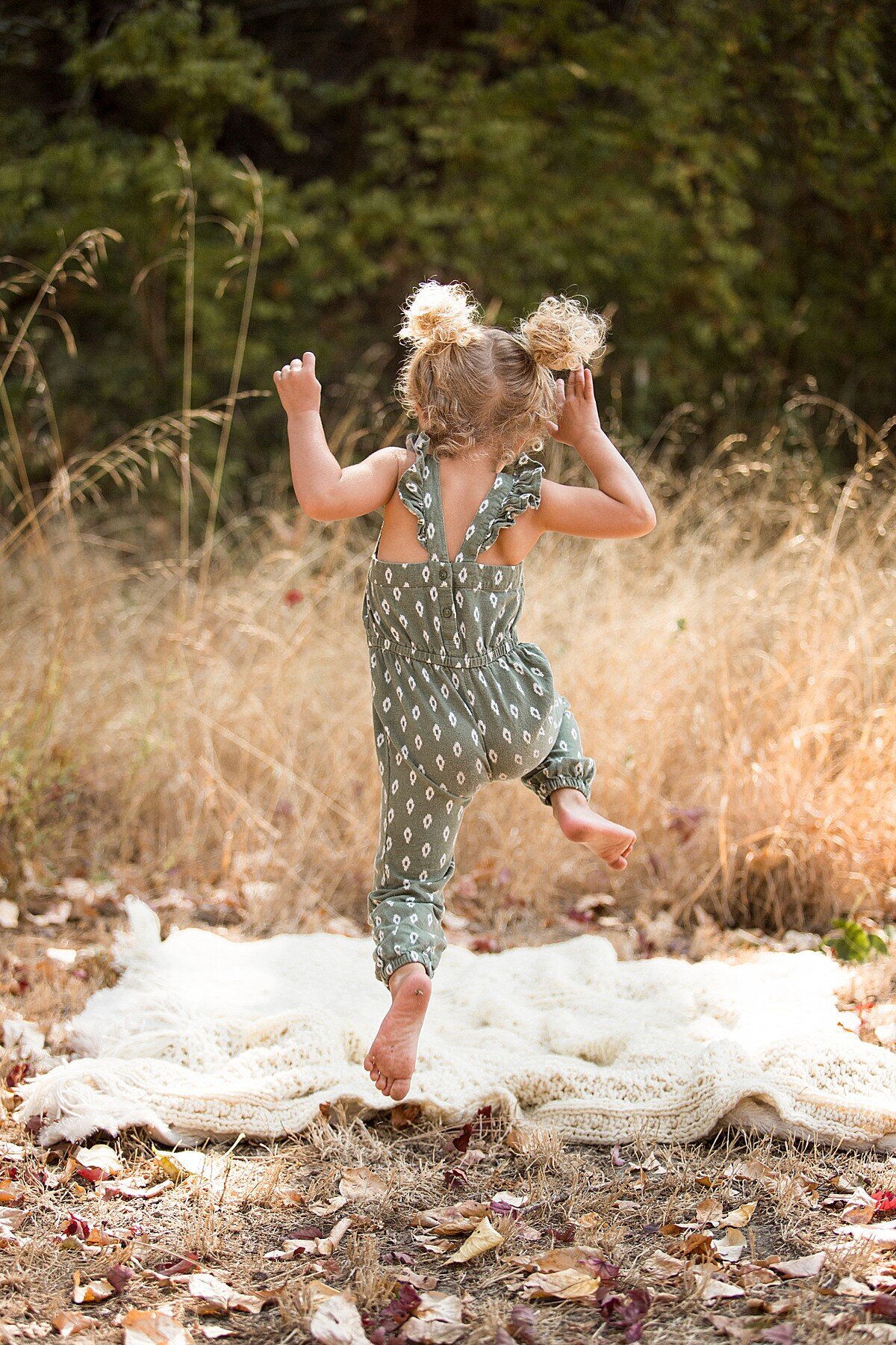 Cute toddler girl with pigtails jumping on a blanket
