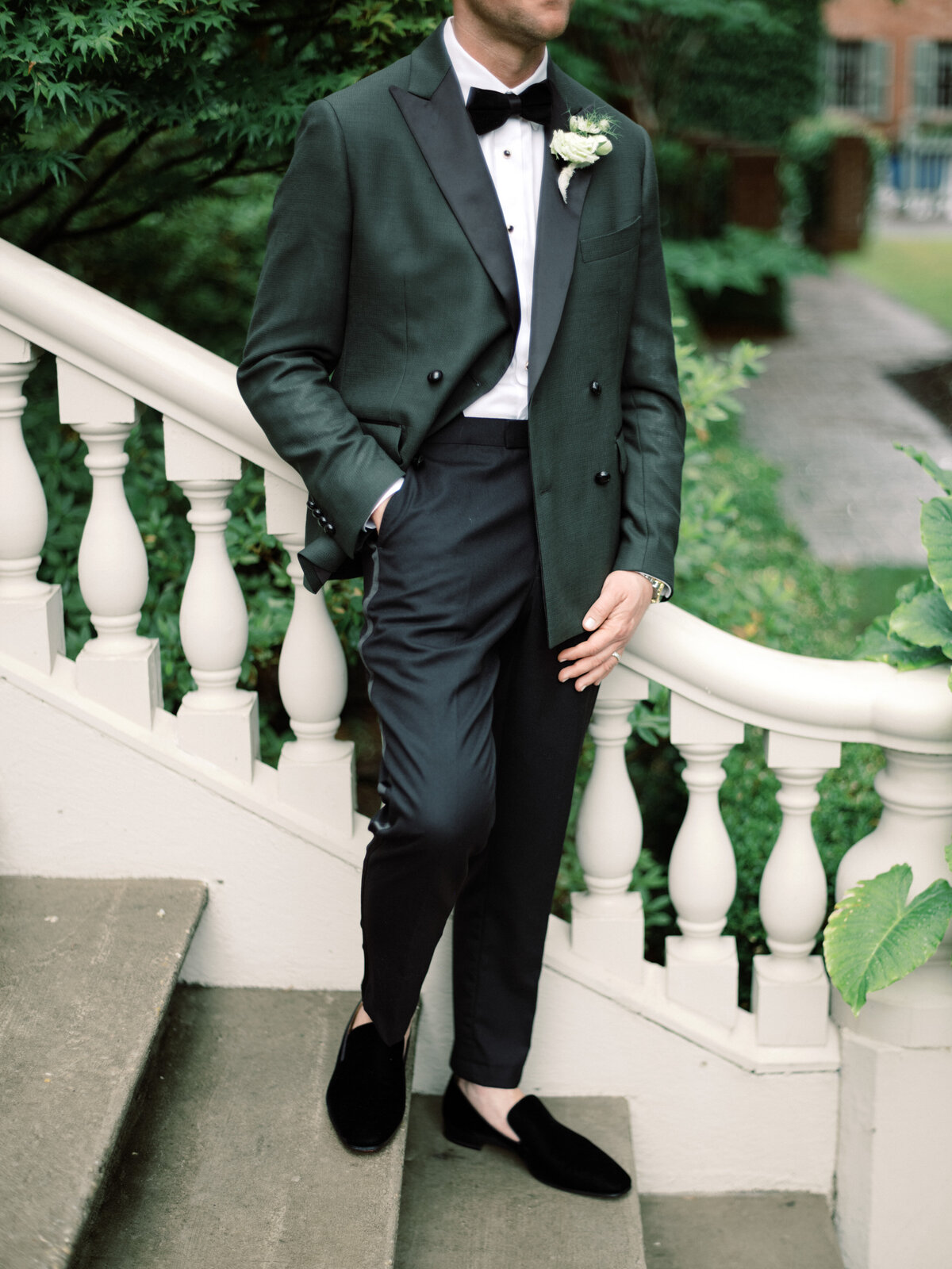 A groom leans casually against a beautiful staircase, showcasing the refinement of his attire, embodying charm and elegance that resonates with wedding bliss and excitement.