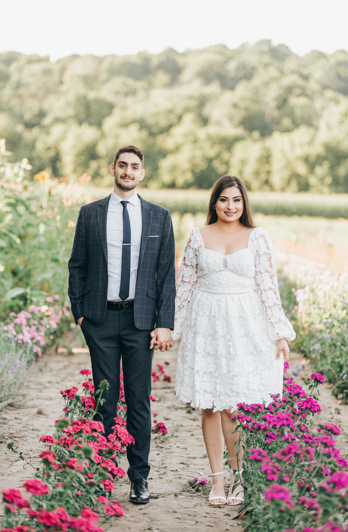 Couple holding hands and walking through a whimsical wildflower field during their Summer engagement session