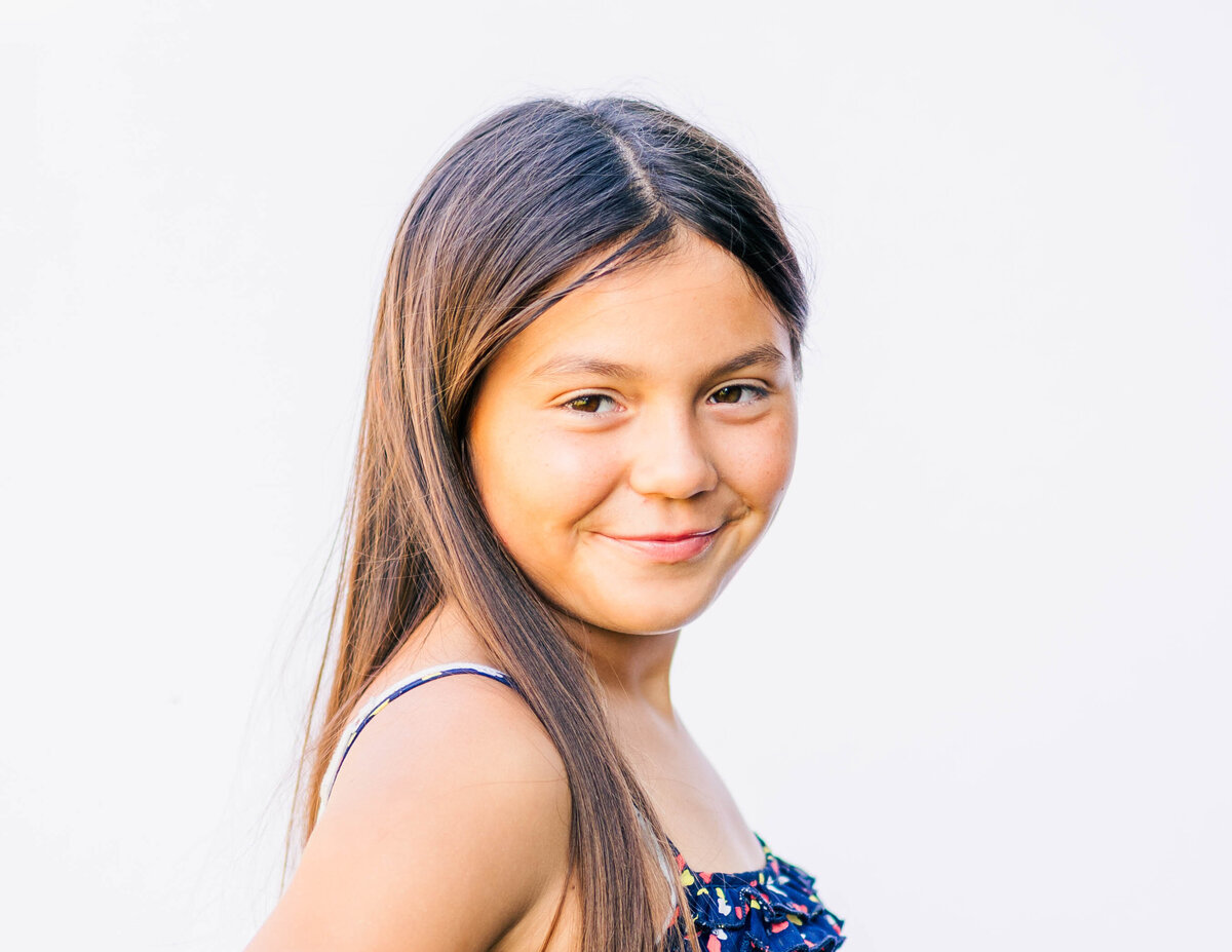 Fine art portrait of 5th-grade girl with bright smile and white backdrop
