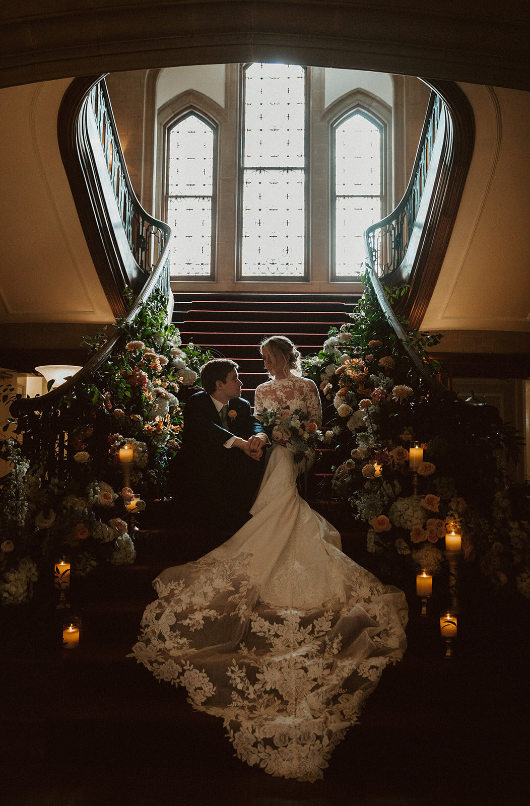 bride and groom sit on stairs surrounded by flowers at callanwolde fine arts center in atlatna 