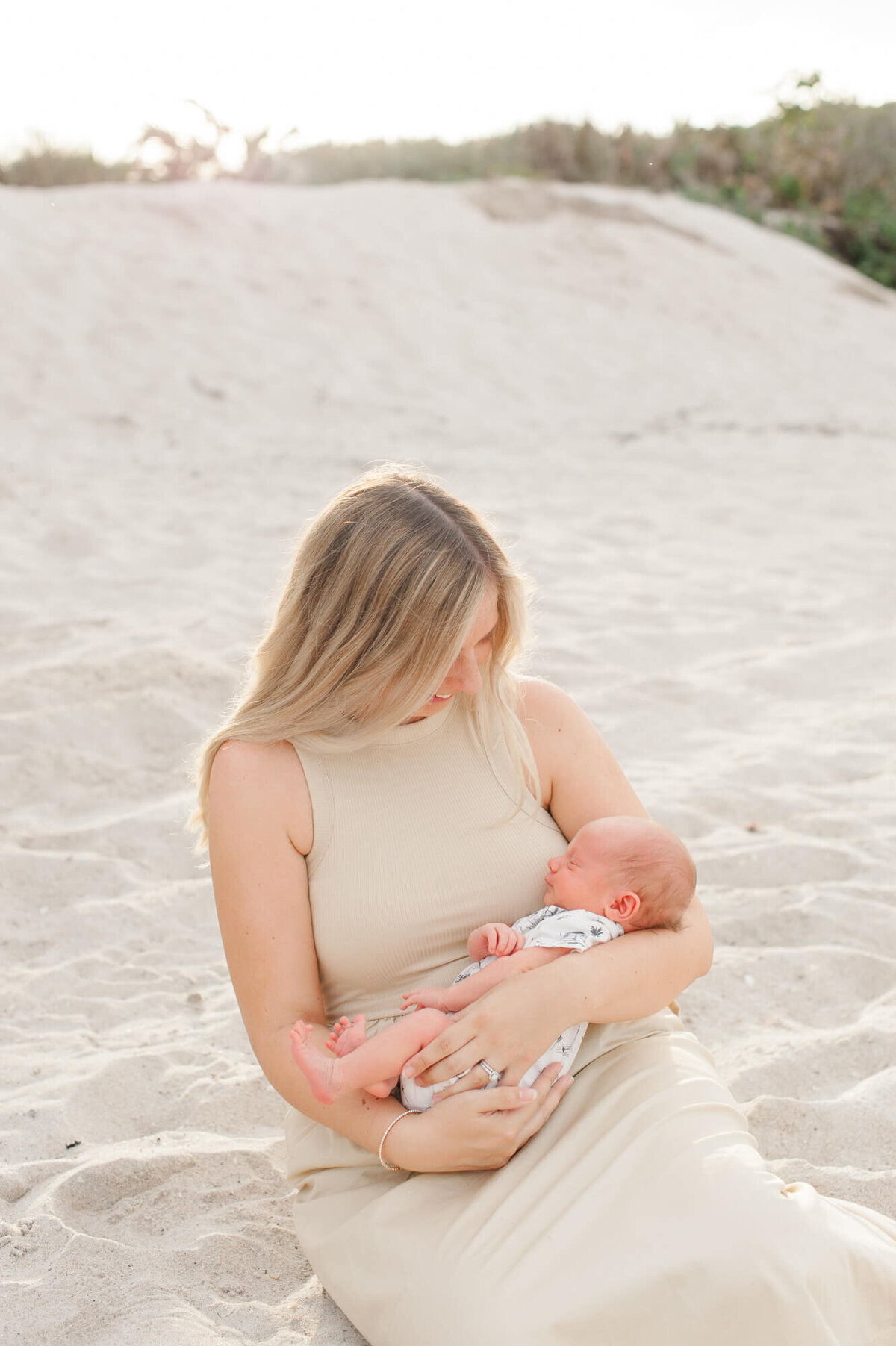 Orlando newborn photographer captures new mom holding her son while sitting in the sand