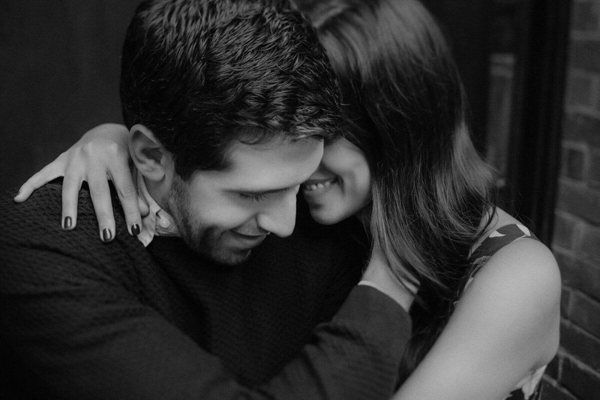 The fiancée is lovingly hugging her fiancé sideways while smiling, in West Village, Manhattan, NYC. Image by Jenny Fu Studio.