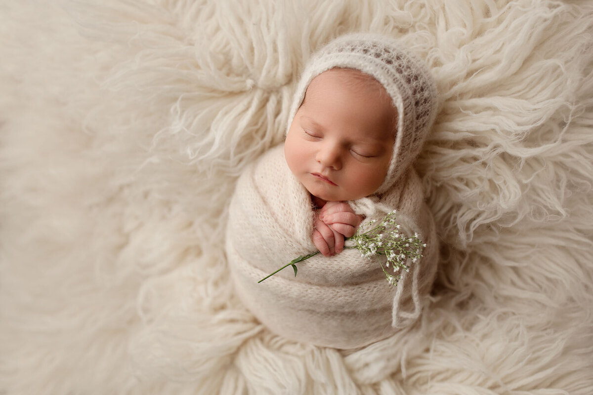 sweek baby girl sleeping swaddled up holding a flower