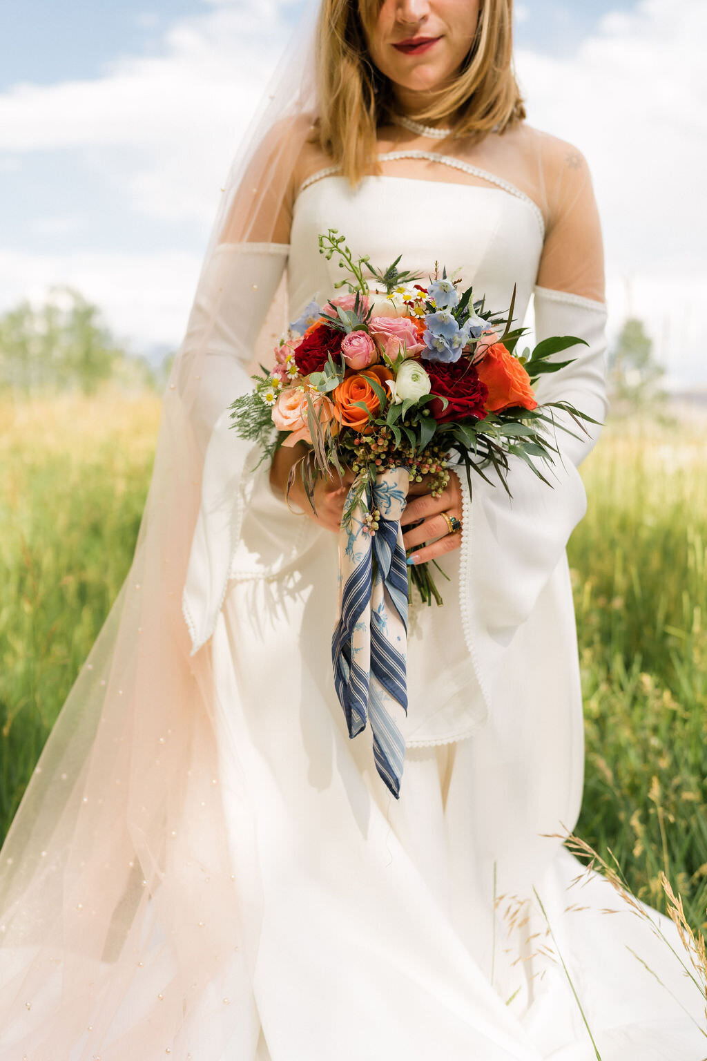 a colorful bouquet of flowers behind held by both hands by a bride