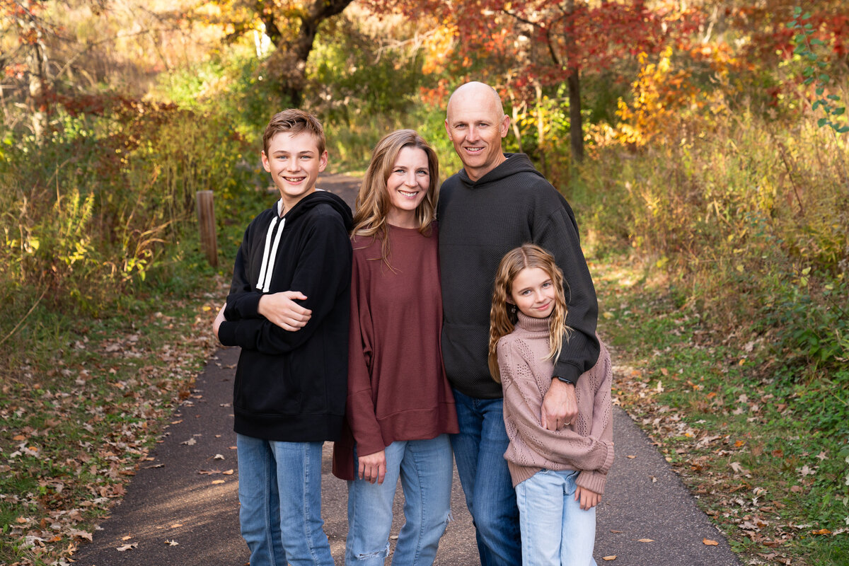 Family of four standing close together in a fall scene for their family photos