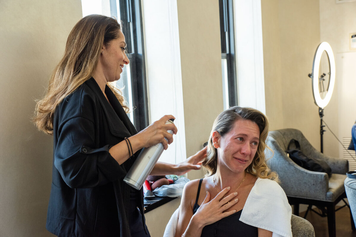 A woman spraying a woman 's hair with a spray bottle