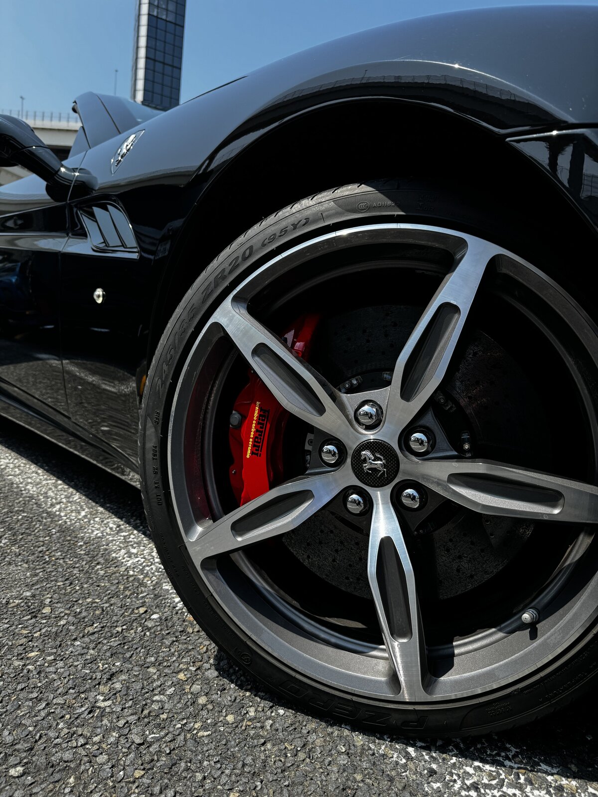 Detailed close-up of a black Ferrari California’s alloy wheel and red brake caliper, showcasing its sleek design and performance aesthetic.