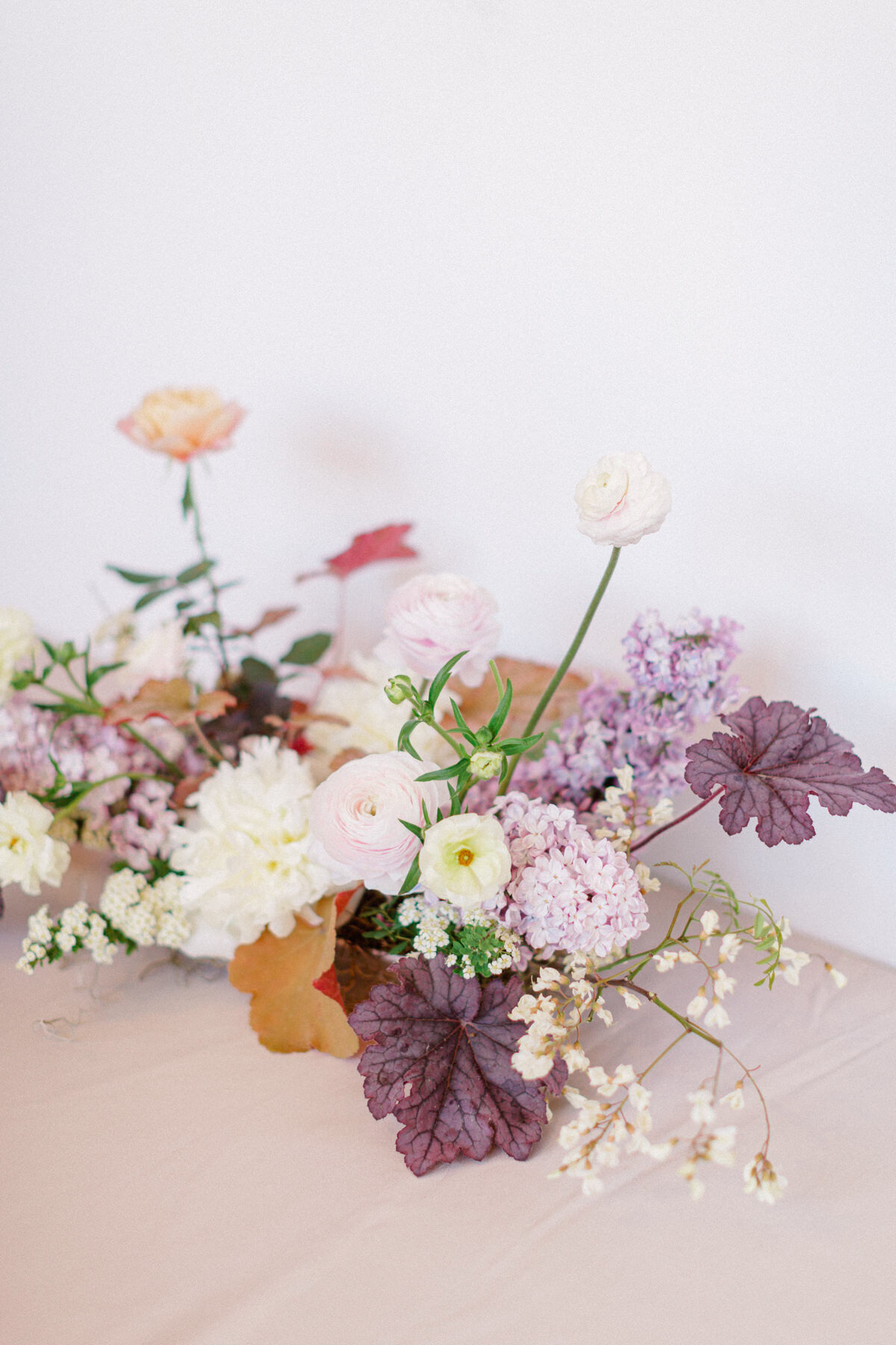 An arrangement of spring flowers featuring lilacs and colourful greenery sits on a table.