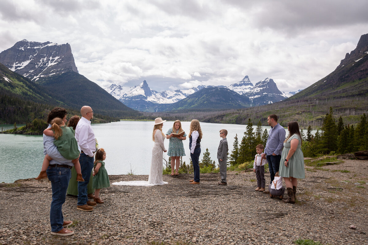 Family and friends stand in a semi-circle around two brides at their elopement ceremony in Montana.