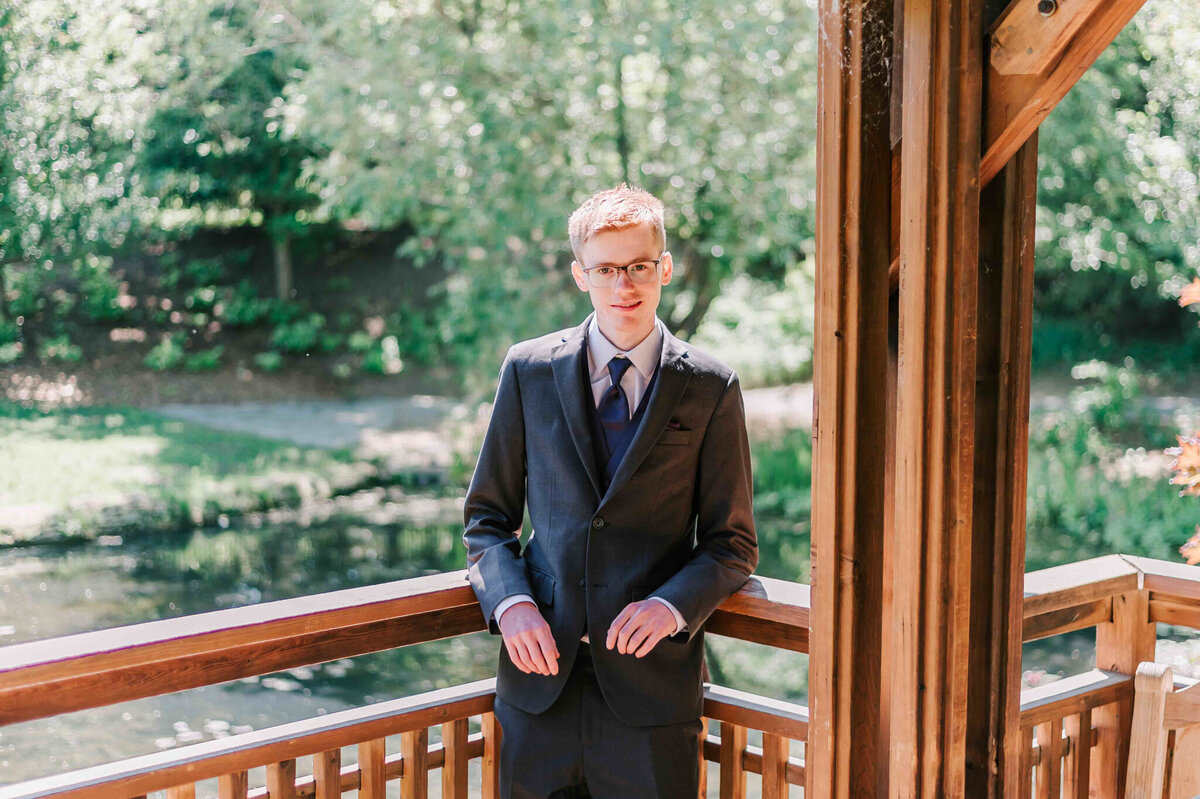 A young blonde man standing against a wood wall of a gazebo.