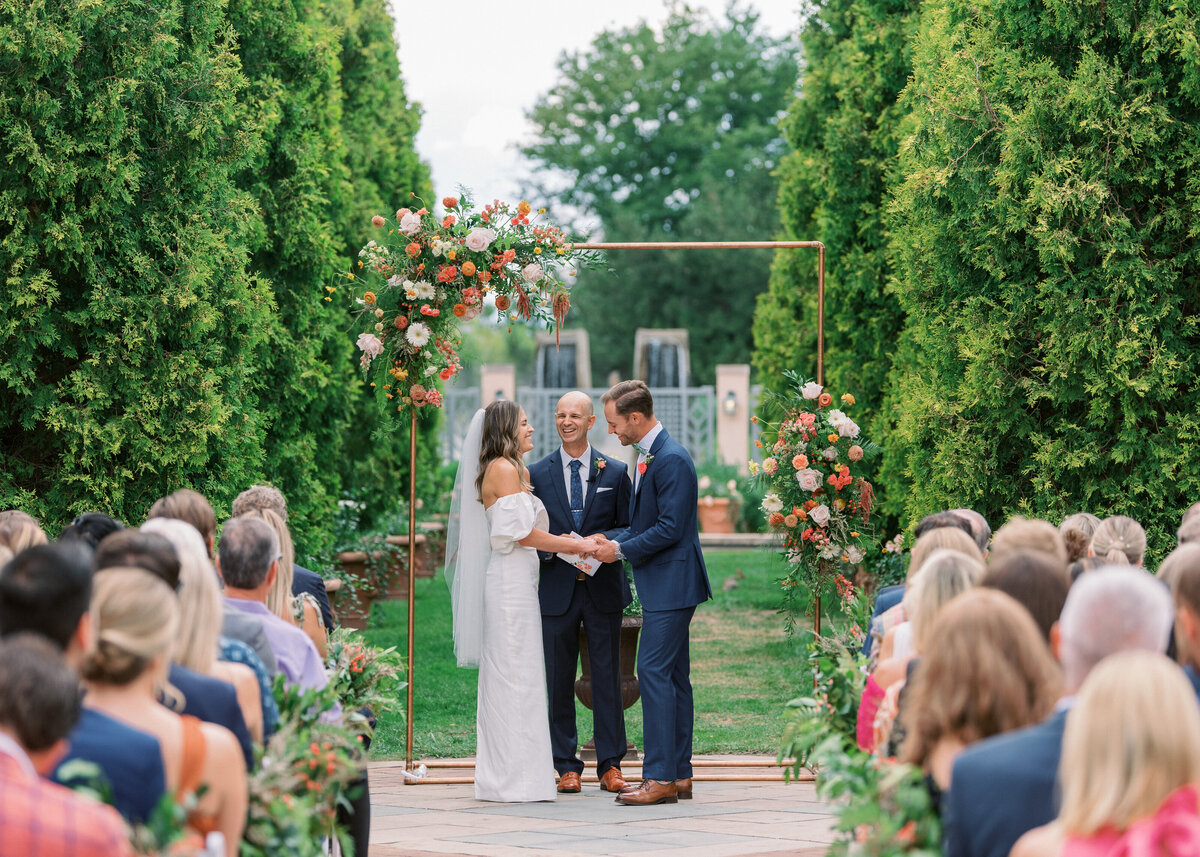 New husband and wife walk through a green garden together while holding hands in an image taken by Virginia Wedding Photographer
