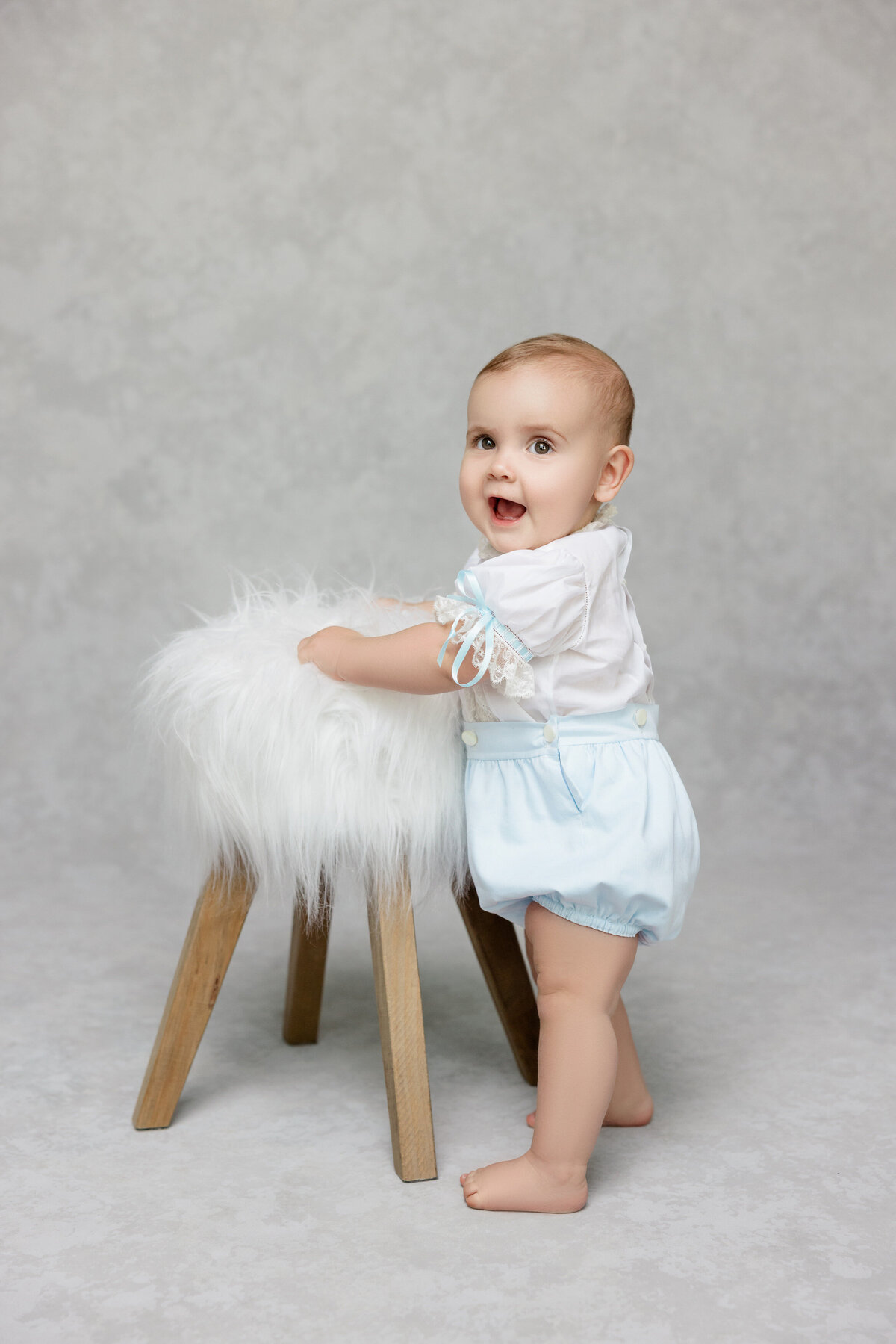 A small baby standing next to a fuzzy stool